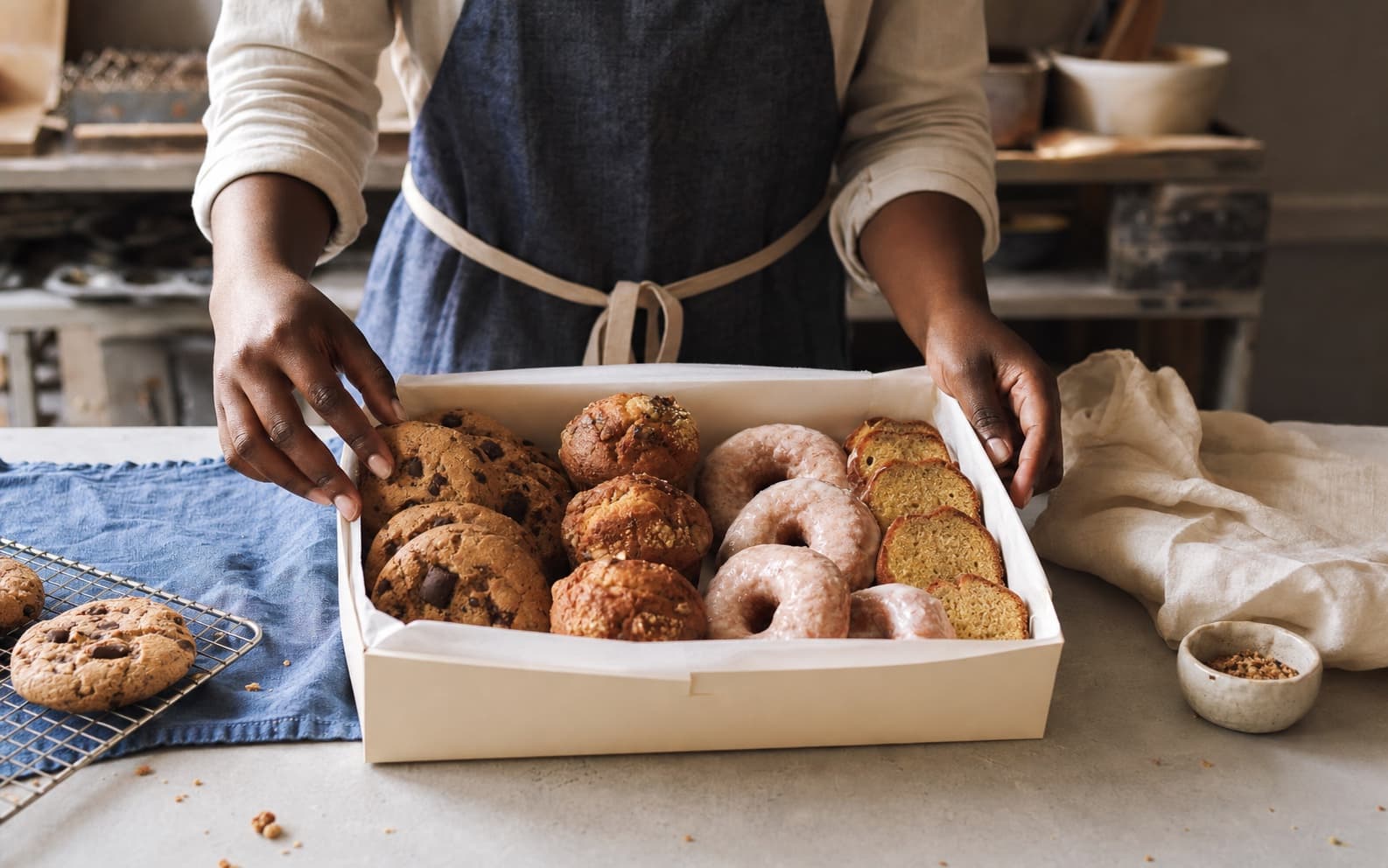 A Maison Shan baker arranging cookies, muffins, doughnuts and loaf cake in a pastry box